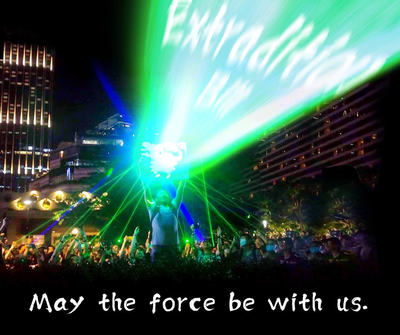 Modified photograph of a protestor holding up a reflector, on which other people are aiming blue and green laser pointers. The beam from the reflector has been edited to read "Extradition Bill" in white. The image is captioned, "May the force be with us."